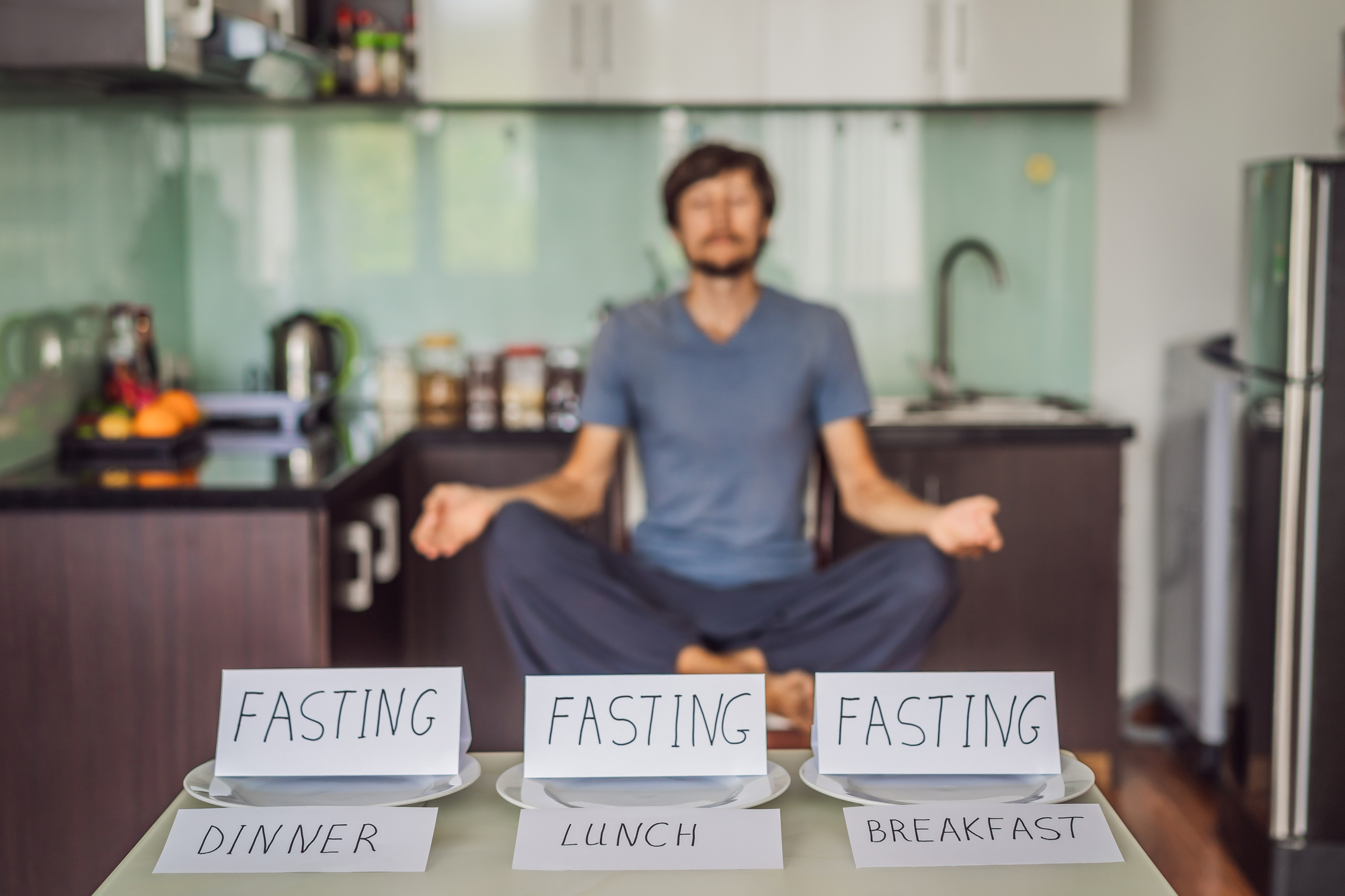 Man sitting cross legged while meditating behind three cards that say "fasting"